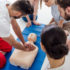 instructor performing cpr on dummy during first aid training with group of people