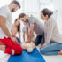 group of people looking at man performing cpr on dummy during first aid training